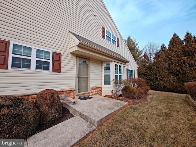 entrance to property with stone siding, a patio area, and a yard