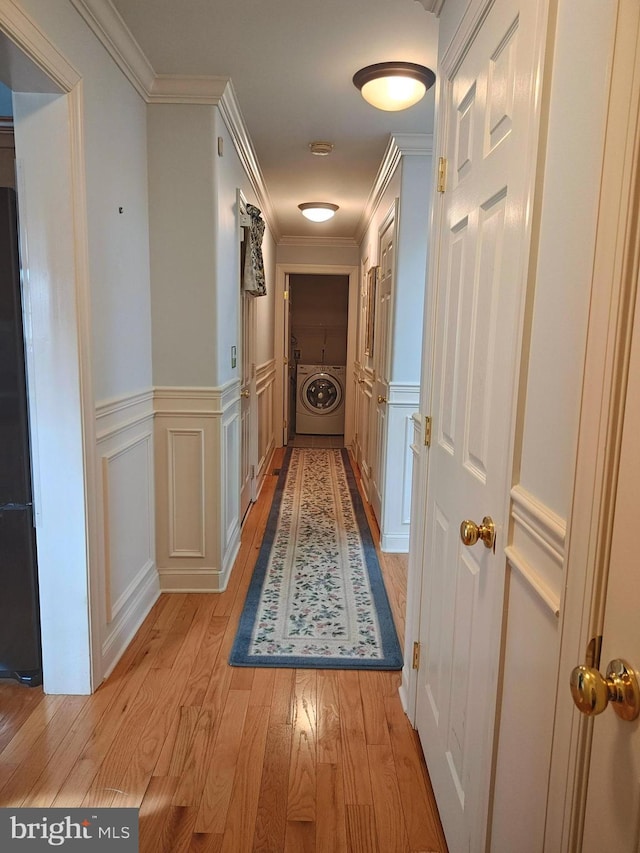 corridor with a wainscoted wall, washer / clothes dryer, crown molding, light wood-type flooring, and a decorative wall