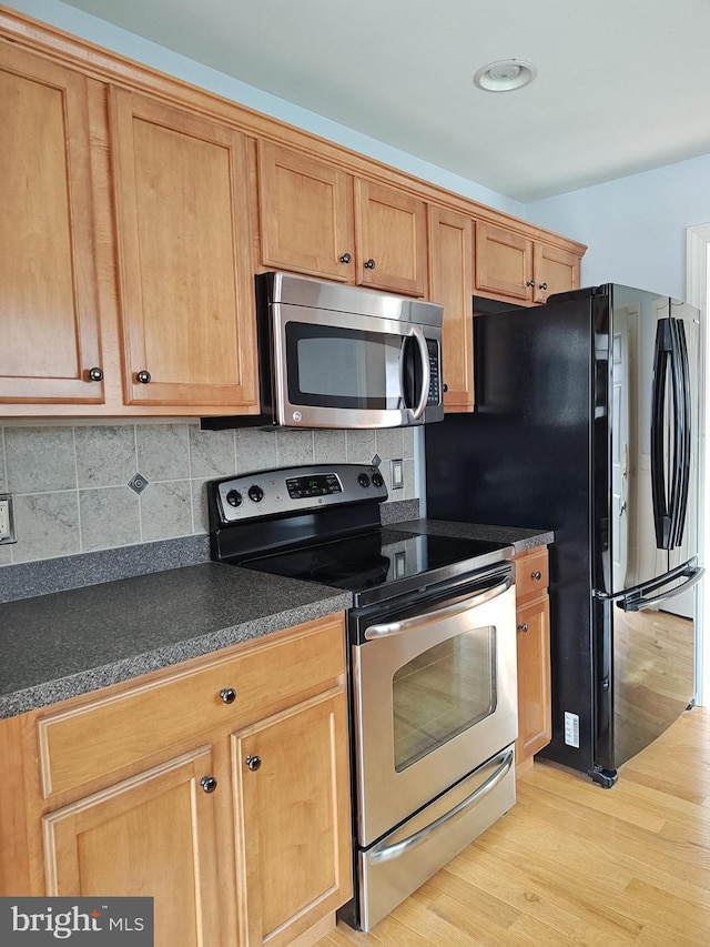 kitchen featuring light wood-type flooring, appliances with stainless steel finishes, dark countertops, and tasteful backsplash