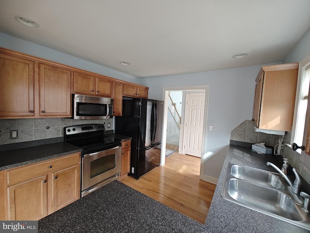 kitchen with stainless steel appliances, dark countertops, tasteful backsplash, a sink, and light wood-type flooring