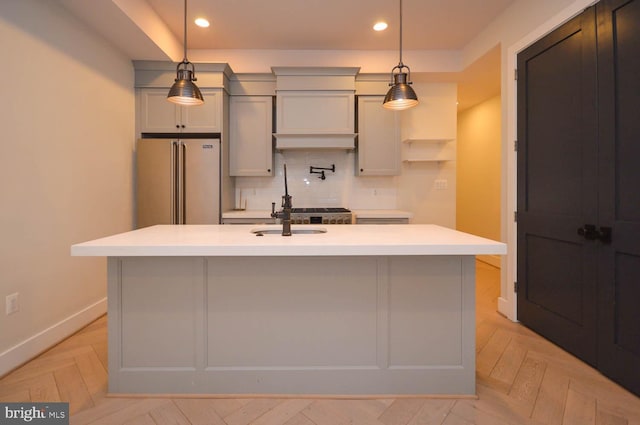 kitchen with a sink, high end fridge, light countertops, decorative backsplash, and an island with sink