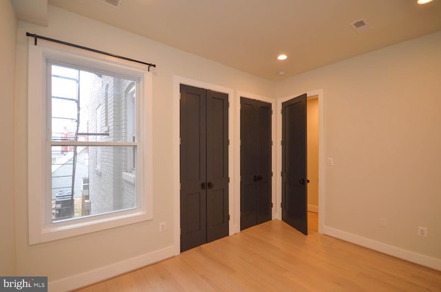 unfurnished bedroom with multiple closets, recessed lighting, baseboards, and wood finished floors