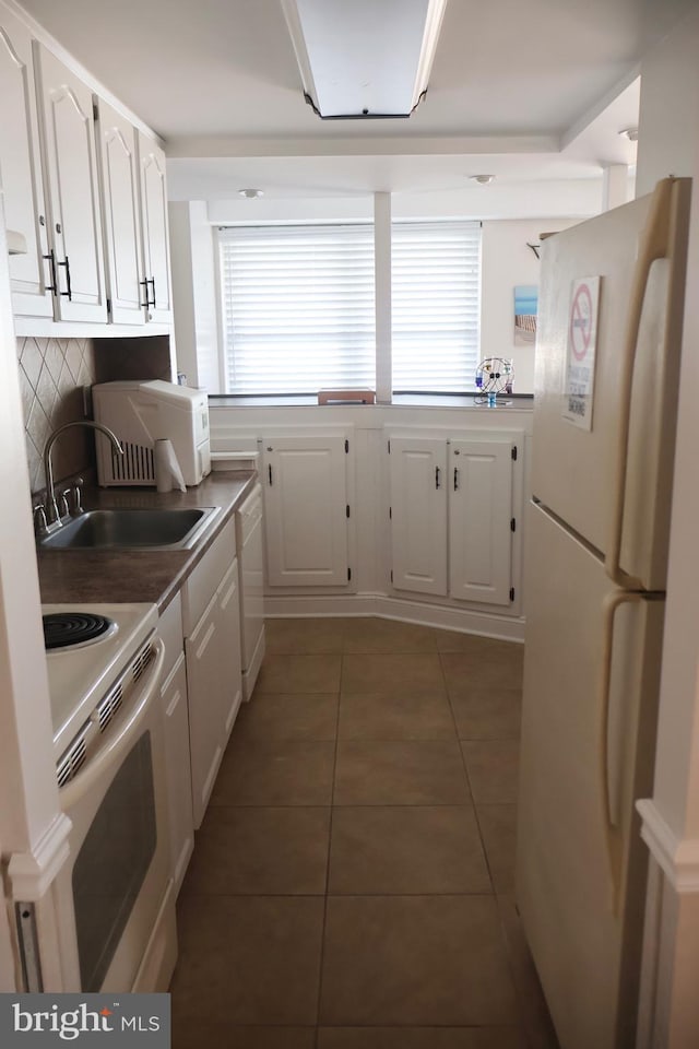 kitchen with dark tile patterned flooring, white appliances, a sink, white cabinetry, and plenty of natural light