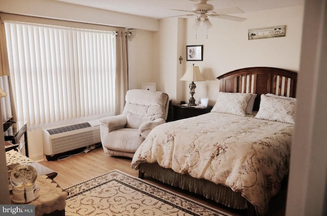 bedroom featuring a wall unit AC, ceiling fan, and wood finished floors