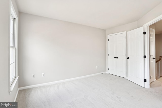 unfurnished bedroom with a closet, light colored carpet, and baseboards