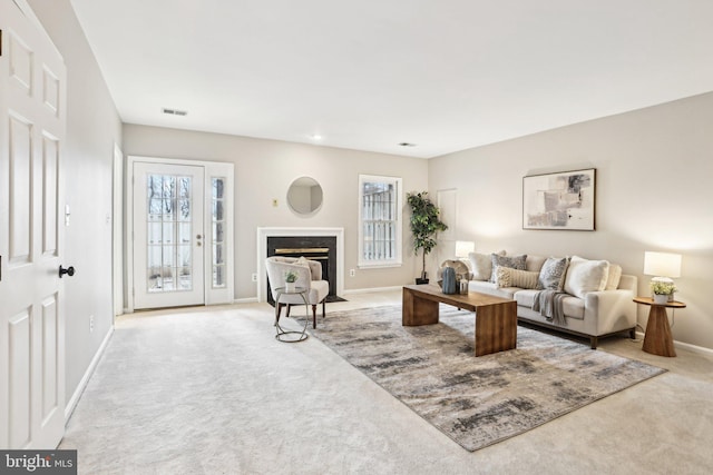 living area featuring a healthy amount of sunlight, carpet, baseboards, and a fireplace with flush hearth