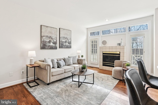 living area with baseboards, a tiled fireplace, and wood finished floors