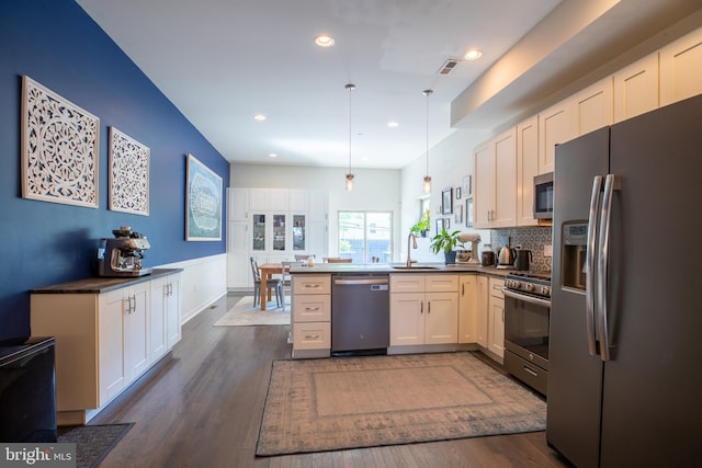 kitchen featuring stainless steel appliances, a sink, white cabinets, dark countertops, and pendant lighting