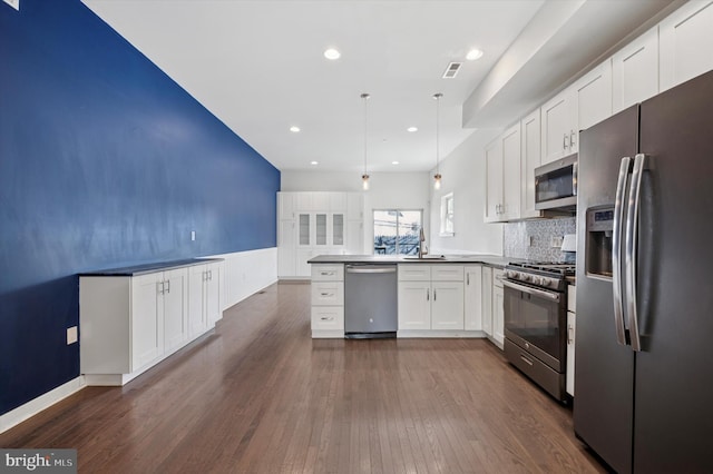 kitchen featuring appliances with stainless steel finishes, decorative light fixtures, a peninsula, white cabinetry, and a sink