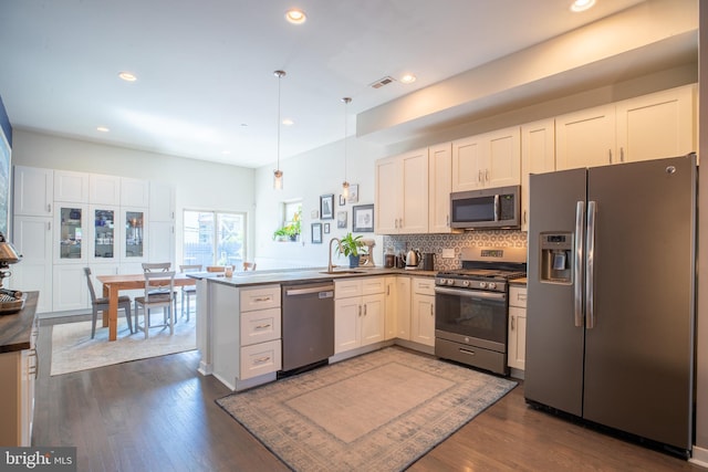 kitchen featuring stainless steel appliances, a peninsula, white cabinetry, dark countertops, and decorative light fixtures