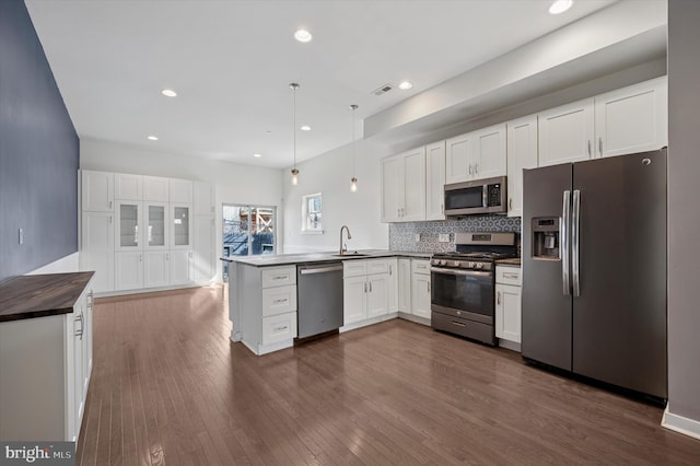 kitchen with dark wood-style floors, decorative light fixtures, appliances with stainless steel finishes, white cabinetry, and a peninsula