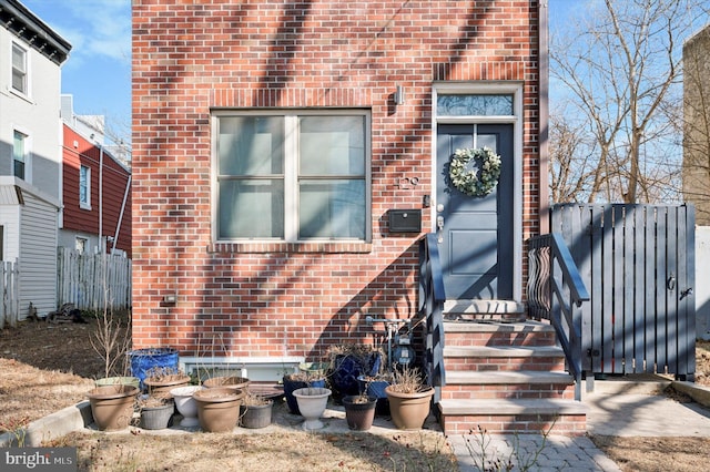 view of exterior entry featuring brick siding and fence