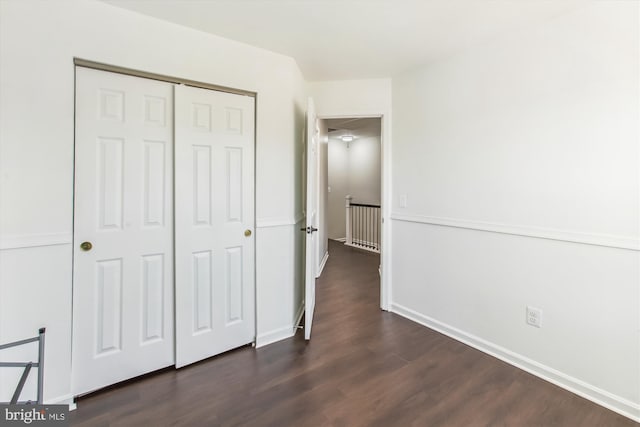 unfurnished bedroom featuring dark wood-type flooring, a closet, and baseboards