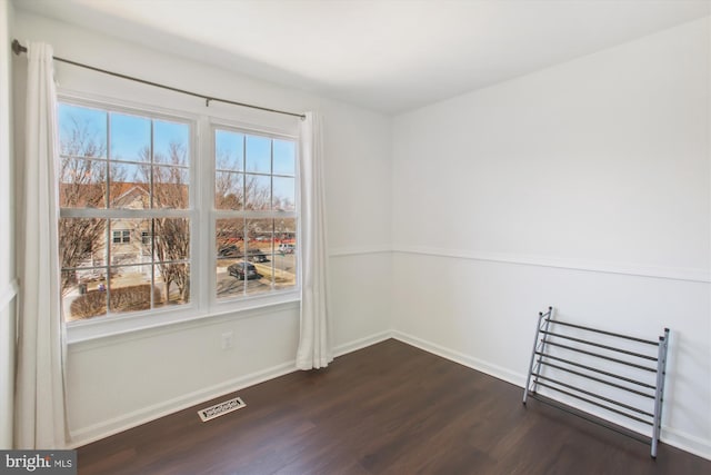 unfurnished room featuring visible vents, dark wood finished floors, and baseboards