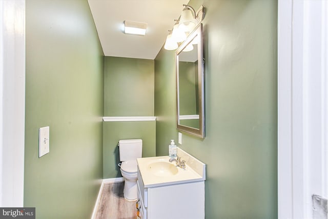 half bath with vanity, wood finished floors, toilet, and baseboards