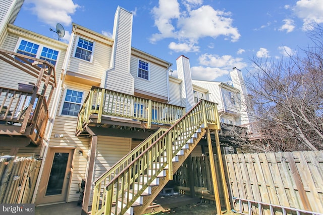 back of property with stairway, a chimney, fence, and a deck