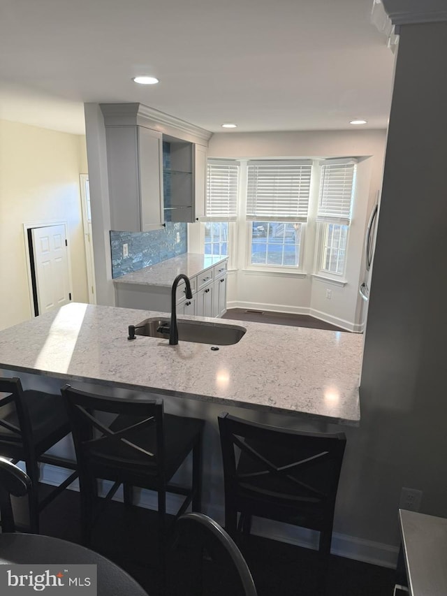 kitchen featuring a kitchen bar, light stone counters, a sink, and recessed lighting