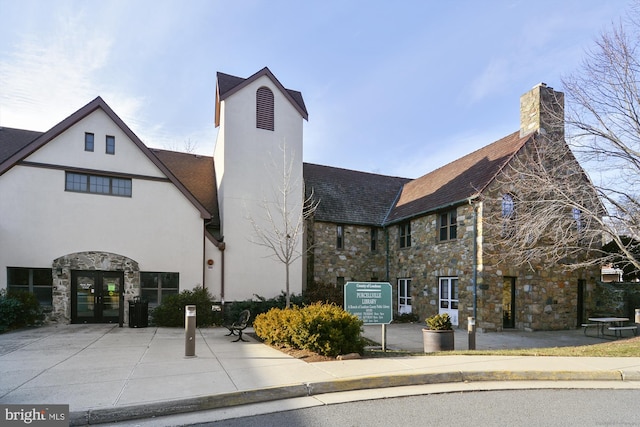 view of front of home featuring stone siding, french doors, a chimney, and stucco siding