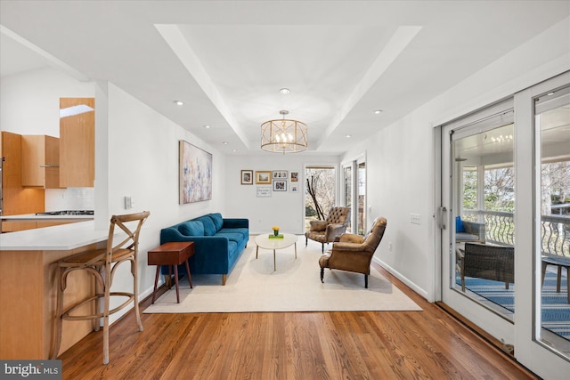 living room featuring baseboards, a raised ceiling, wood finished floors, a notable chandelier, and recessed lighting