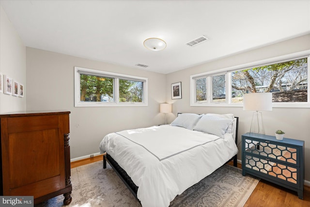 bedroom with multiple windows, wood finished floors, visible vents, and baseboards