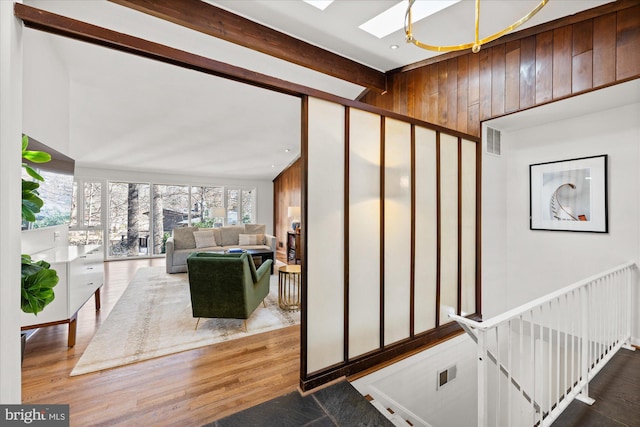 interior space with vaulted ceiling with skylight, wood walls, wood finished floors, and visible vents