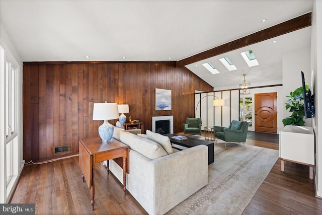 living area featuring lofted ceiling with skylight, wooden walls, visible vents, and wood finished floors