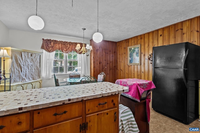 kitchen with freestanding refrigerator, pendant lighting, light countertops, and wooden walls