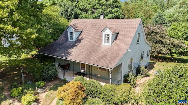 view of front of house with a shingled roof, a patio area, and a view of trees