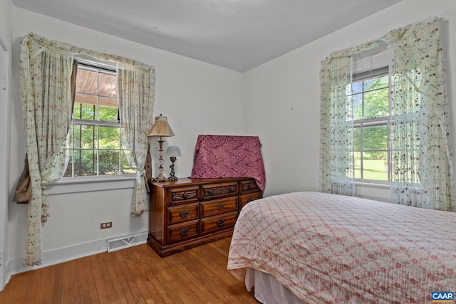 bedroom with baseboards, multiple windows, visible vents, and wood finished floors