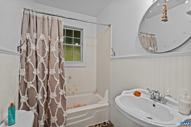 bathroom with toilet, shower / bath combo, a sink, and wainscoting