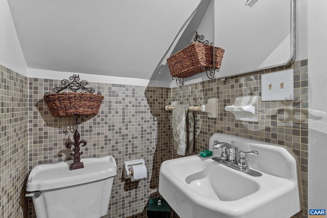 half bath with toilet, a sink, and tile walls