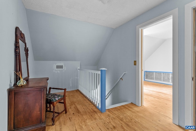 bonus room featuring vaulted ceiling, light wood-style flooring, a textured ceiling, and visible vents