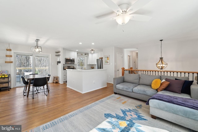 living room with light wood-style flooring, ceiling fan with notable chandelier, baseboards, and recessed lighting