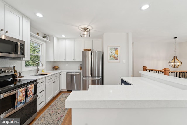 kitchen featuring pendant lighting, stainless steel appliances, light wood-style flooring, white cabinetry, and a sink