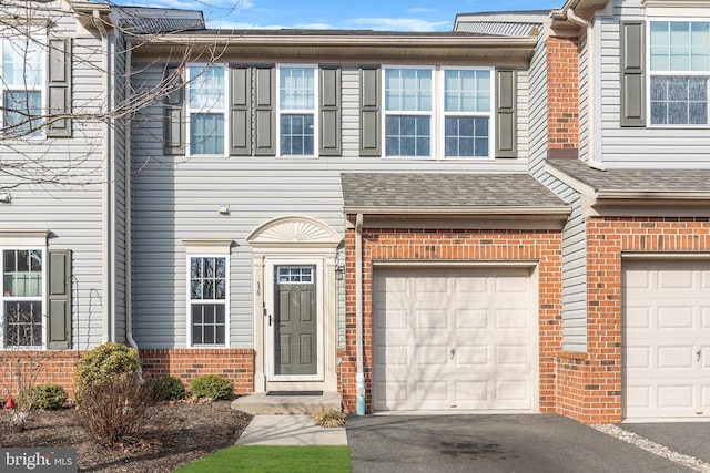 multi unit property featuring an attached garage, driveway, roof with shingles, and brick siding