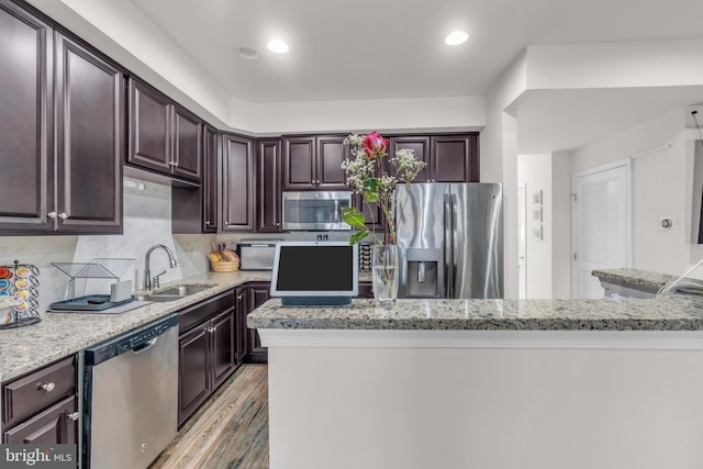 kitchen featuring stainless steel appliances, a sink, light wood finished floors, and dark brown cabinets