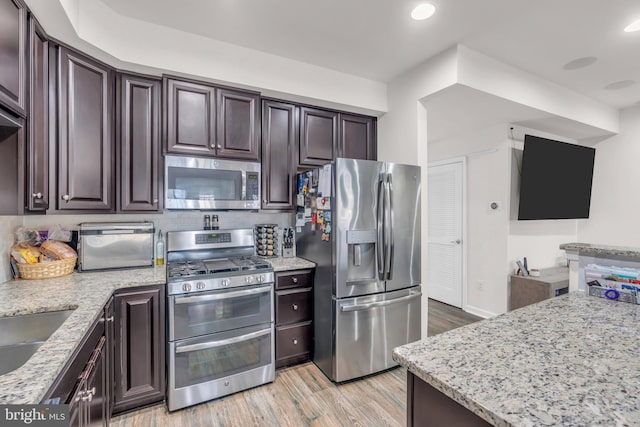 kitchen with stainless steel appliances, light wood-style flooring, dark brown cabinetry, and light stone countertops