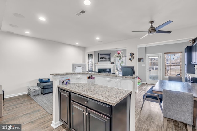 kitchen featuring a center island with sink, visible vents, open floor plan, light stone countertops, and light wood-type flooring