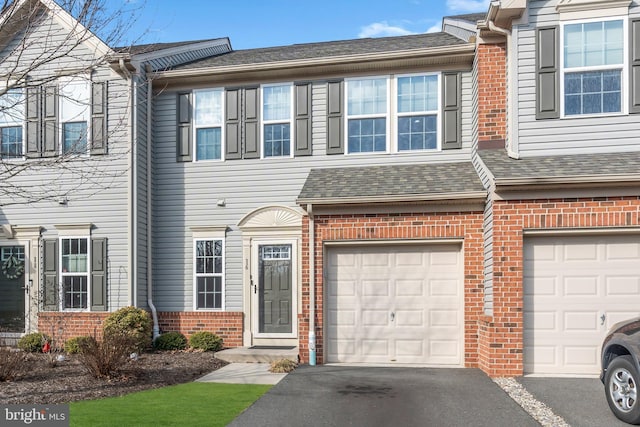 view of property featuring a garage, brick siding, roof with shingles, and aphalt driveway