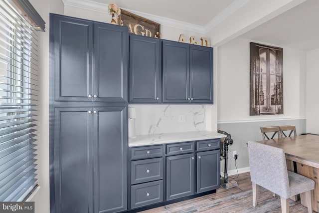 kitchen with light wood-style flooring, baseboards, blue cabinetry, light stone countertops, and crown molding