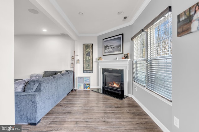 living area featuring wood finished floors, visible vents, baseboards, a glass covered fireplace, and crown molding