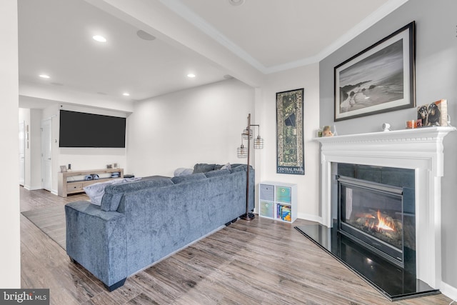 living room with recessed lighting, light wood-style flooring, ornamental molding, a glass covered fireplace, and baseboards