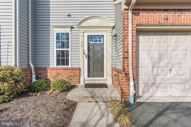 doorway to property featuring a garage, brick siding, and aphalt driveway