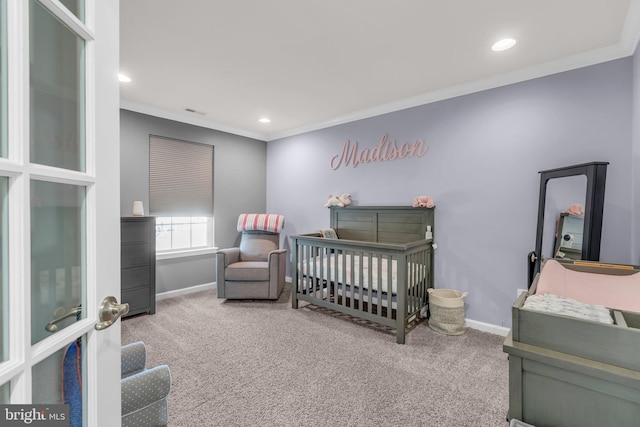 carpeted bedroom featuring a crib, visible vents, baseboards, and crown molding