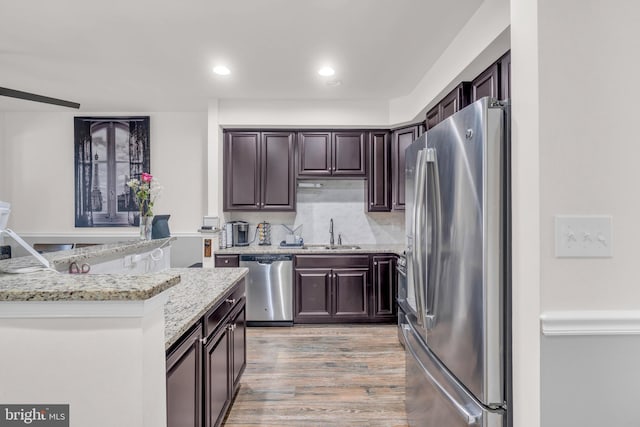 kitchen featuring a sink, light stone counters, stainless steel appliances, and dark brown cabinets