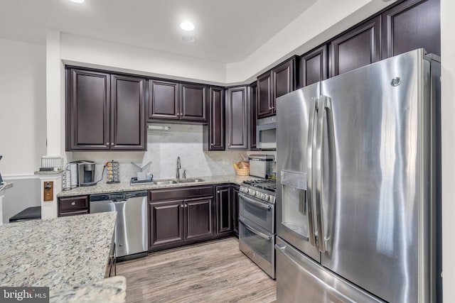 kitchen with light wood-style flooring, appliances with stainless steel finishes, a sink, dark brown cabinetry, and light stone countertops