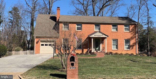 colonial inspired home featuring driveway, fence, a front yard, brick siding, and a chimney