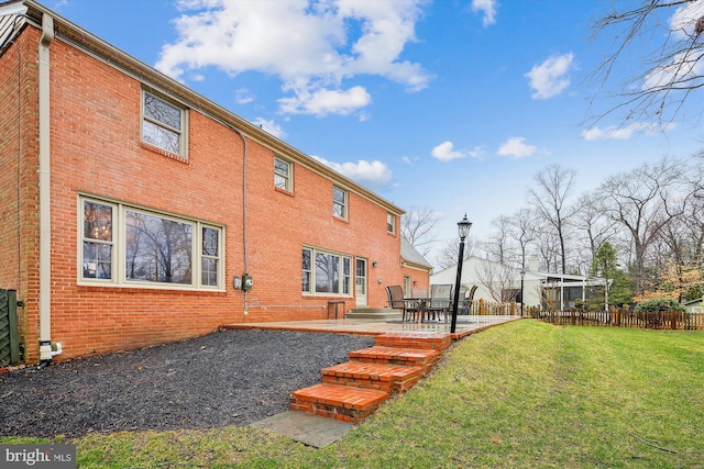 rear view of house with a patio, a yard, fence, and brick siding