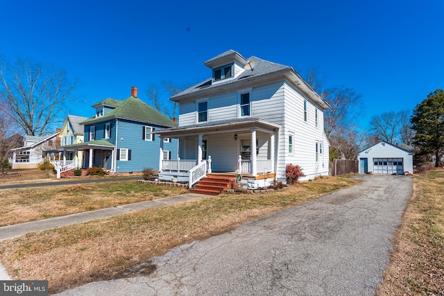 american foursquare style home with aphalt driveway, covered porch, an outdoor structure, a detached garage, and a front yard