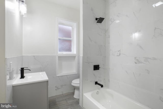 bathroom featuring toilet, shower / washtub combination, tile walls, and vanity